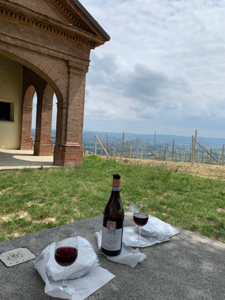 Dettaglio del picnic panini e bottiglia di vino con vista vigne e cappella.